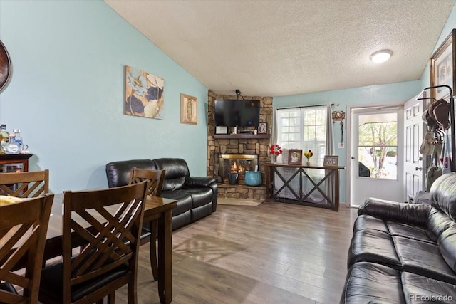 living room featuring a stone fireplace, a textured ceiling, hardwood / wood-style floors, and vaulted ceiling