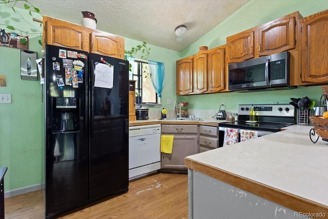 kitchen featuring light hardwood / wood-style floors, vaulted ceiling, sink, stainless steel appliances, and a textured ceiling