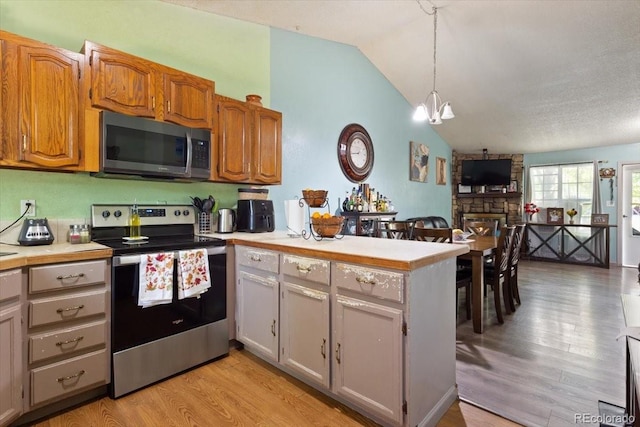 kitchen featuring hanging light fixtures, a stone fireplace, vaulted ceiling, appliances with stainless steel finishes, and light hardwood / wood-style floors