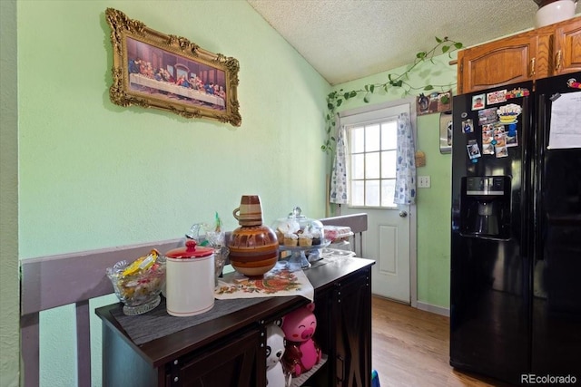 kitchen featuring lofted ceiling, light hardwood / wood-style flooring, black fridge with ice dispenser, and a textured ceiling