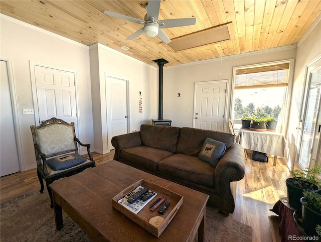 living area with wood finished floors, wood ceiling, a ceiling fan, ornamental molding, and a wood stove