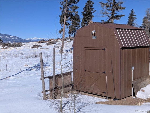 snow covered structure featuring a storage unit, a mountain view, and an outdoor structure