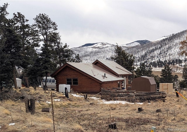 view of property exterior featuring a mountain view, a storage unit, an outdoor structure, and log exterior