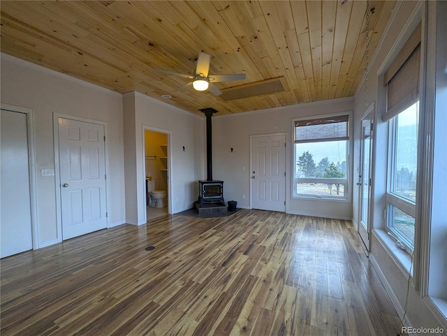 unfurnished living room featuring baseboards, ceiling fan, wood finished floors, a wood stove, and wooden ceiling