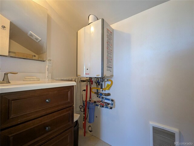 bathroom featuring tankless water heater, visible vents, lofted ceiling, and vanity