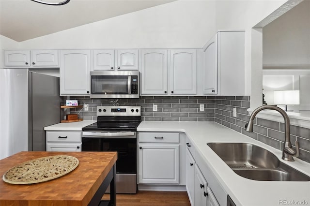 12753 Buckhorn Creek St, Parker, CO 80134 - kitchen featuring appliances with stainless steel finishes, a sink, vaulted ceiling, white cabinets, and decorative backsplash