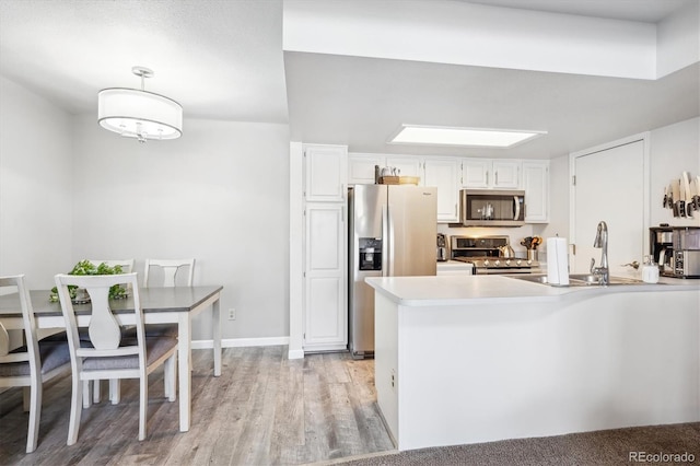 kitchen featuring a peninsula, light wood-style flooring, stainless steel appliances, light countertops, and white cabinetry