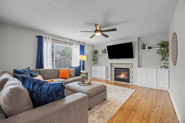 11188 Latigo Ln, Parker, CO 80138 - living room featuring light wood finished floors, a ceiling fan, a fireplace with flush hearth, a textured ceiling, and baseboards