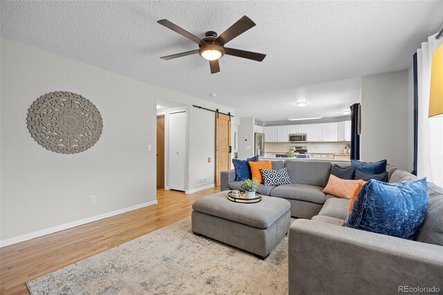 11188 Latigo Ln, Parker, CO 80138 - living area with light wood-style floors, a ceiling fan, a barn door, baseboards, and a textured ceiling