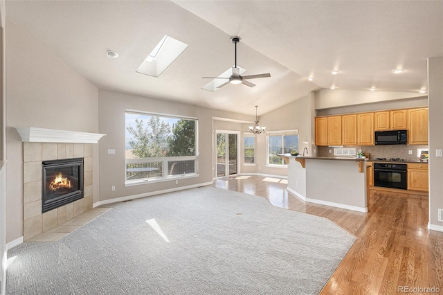 149 Walters Creek Dr, Monument, CO 80132 - unfurnished living room featuring vaulted ceiling, a tile fireplace, light wood-style floors, a chandelier, and a skylight