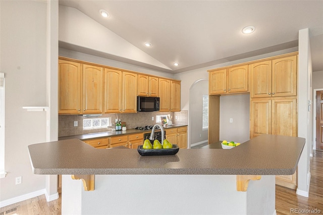149 Walters Creek Dr, Monument, CO 80132 - kitchen featuring black microwave, vaulted ceiling, recessed lighting, tasteful backsplash, and a breakfast bar area