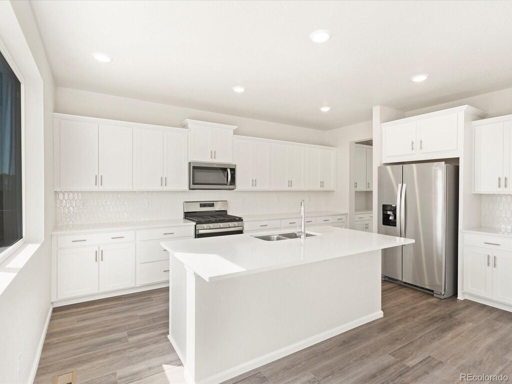 kitchen featuring white cabinetry, light wood-type flooring, a sink, a kitchen island with sink, and appliances with stainless steel finishes