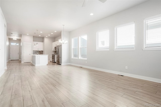 unfurnished living room with sink, ceiling fan with notable chandelier, and light wood-type flooring