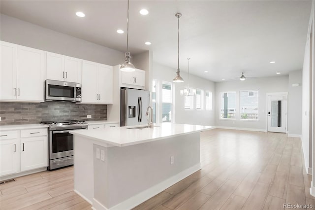 kitchen with appliances with stainless steel finishes, hanging light fixtures, an island with sink, white cabinetry, and ceiling fan with notable chandelier