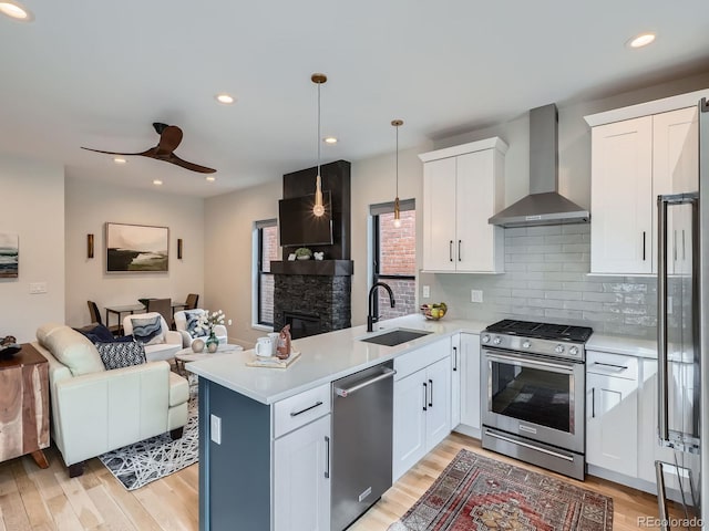 kitchen featuring stainless steel appliances, open floor plan, a sink, wall chimney range hood, and a peninsula