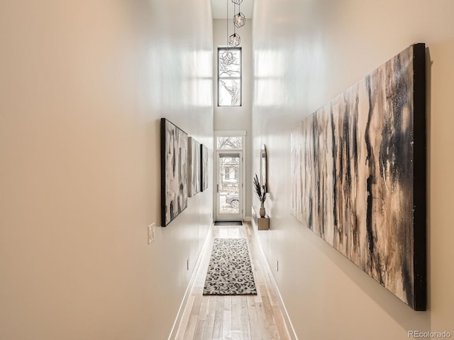 corridor with a towering ceiling, baseboards, and wood finished floors