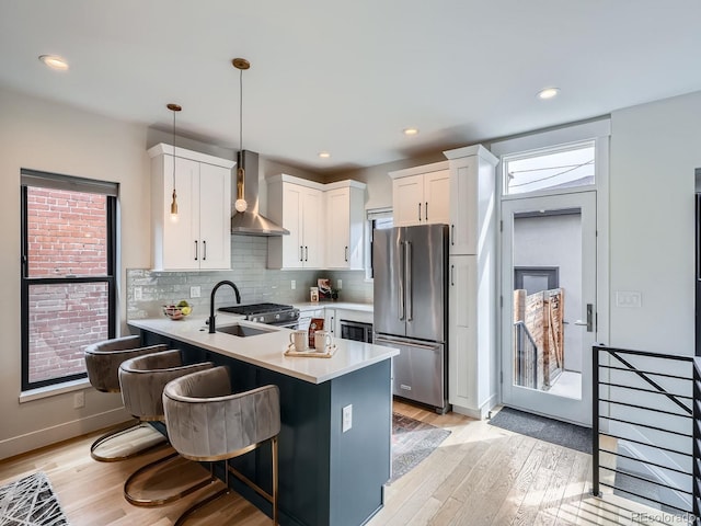 kitchen with light countertops, high quality fridge, wall chimney range hood, a sink, and a peninsula