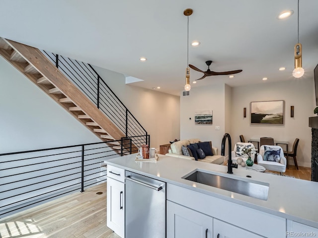 kitchen with light wood-style flooring, open floor plan, hanging light fixtures, a sink, and stainless steel dishwasher