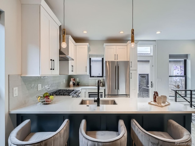 kitchen featuring freestanding refrigerator, hanging light fixtures, a sink, light countertops, and backsplash