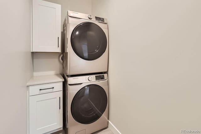 washroom featuring stacked washing maching and dryer, cabinet space, and baseboards