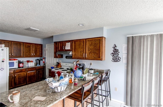 kitchen featuring a kitchen breakfast bar, dark stone counters, a textured ceiling, and white appliances