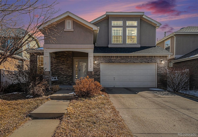 traditional-style house featuring driveway, brick siding, an attached garage, and stucco siding