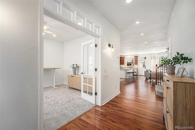 corridor featuring a textured wall, dark wood-type flooring, a textured ceiling, baseboards, and stairs