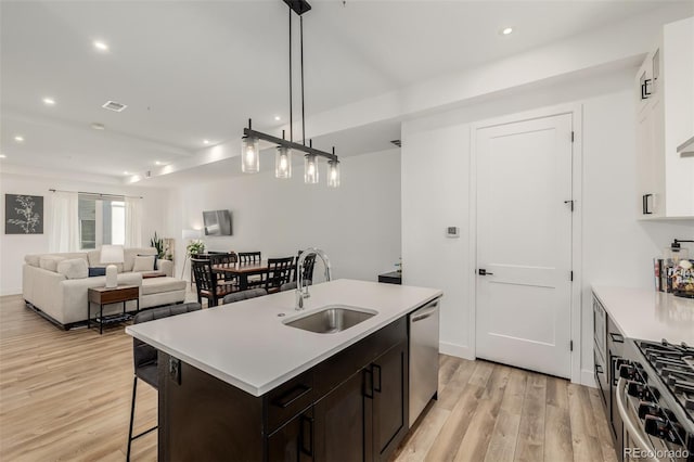 kitchen with sink, appliances with stainless steel finishes, decorative light fixtures, light hardwood / wood-style floors, and dark brown cabinetry