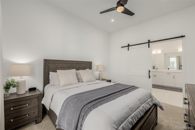 bedroom with ensuite bath, ceiling fan, light colored carpet, and a barn door