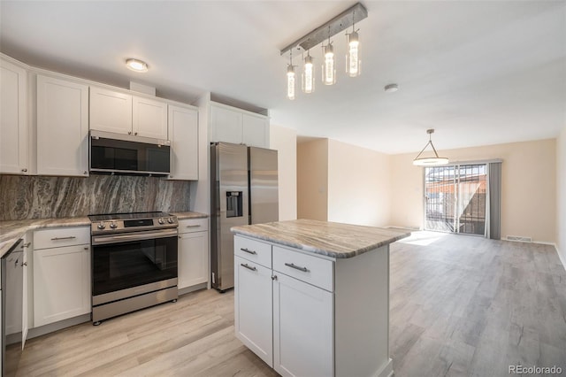 kitchen with tasteful backsplash, decorative light fixtures, appliances with stainless steel finishes, a kitchen island, and white cabinets