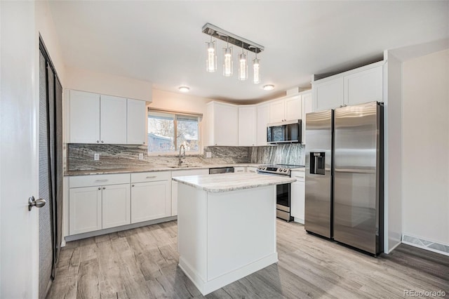 kitchen with appliances with stainless steel finishes, a center island, white cabinets, and decorative light fixtures