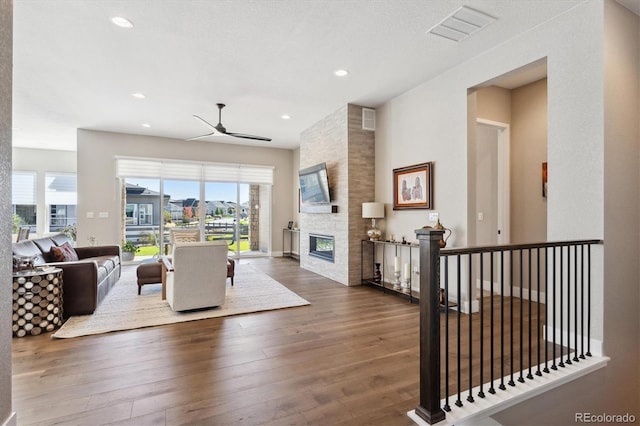 living area with a wealth of natural light, a stone fireplace, wood finished floors, and visible vents