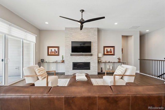 living area with a ceiling fan, recessed lighting, a stone fireplace, and wood finished floors