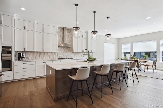 kitchen featuring a breakfast bar, a sink, white cabinets, wall chimney range hood, and a large island