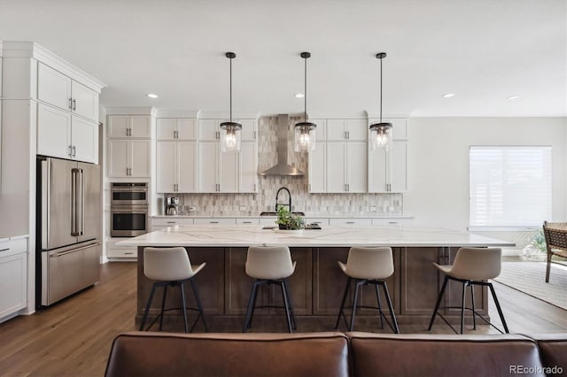 kitchen with a spacious island, hanging light fixtures, appliances with stainless steel finishes, wall chimney range hood, and a kitchen bar