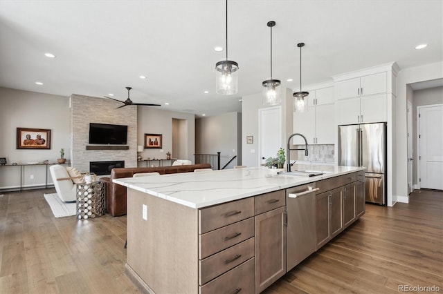 kitchen featuring a kitchen island with sink, stainless steel appliances, white cabinets, open floor plan, and pendant lighting