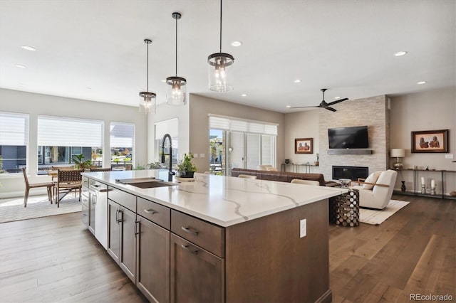 kitchen featuring light stone counters, decorative light fixtures, a large fireplace, a kitchen island with sink, and a sink