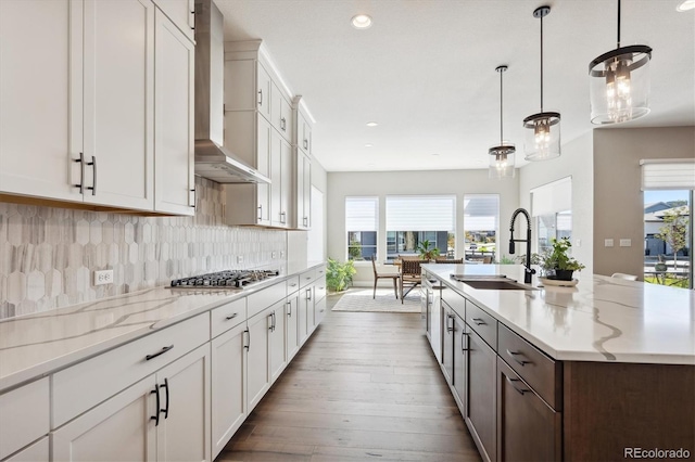 kitchen with an island with sink, decorative light fixtures, wall chimney range hood, stainless steel gas cooktop, and a sink