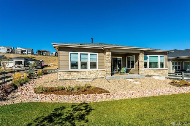 back of house with stone siding, a yard, fence, and a residential view