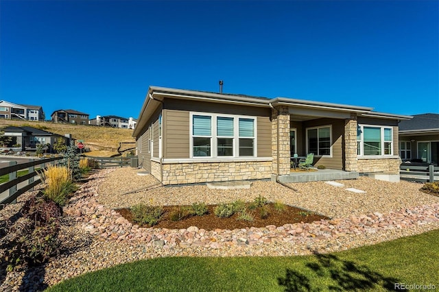 back of house featuring stone siding and fence