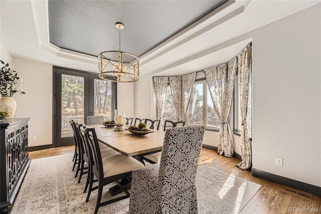 dining space featuring baseboards, visible vents, a tray ceiling, light wood-style floors, and a chandelier