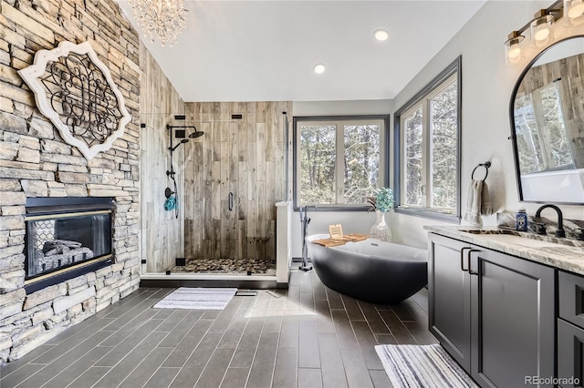 full bathroom featuring vanity, wood tiled floor, a freestanding tub, a stone fireplace, and a shower stall