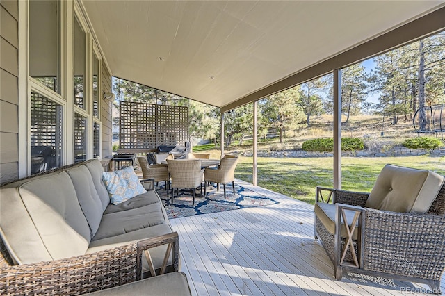 deck with an outdoor living space, a trampoline, outdoor dining space, and a lawn