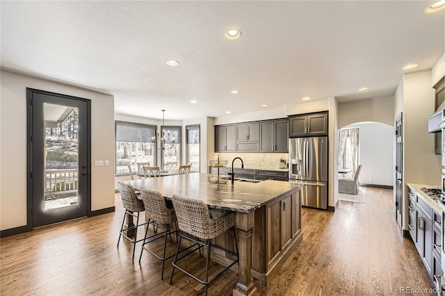 kitchen featuring stainless steel fridge with ice dispenser, arched walkways, dark wood-style flooring, a sink, and tasteful backsplash