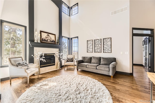 living room with visible vents, wood finished floors, a fireplace, baseboards, and a towering ceiling