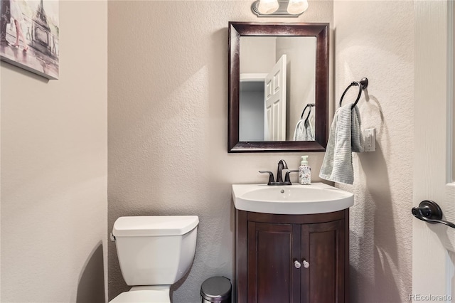 half bath featuring toilet, vanity, and a textured wall