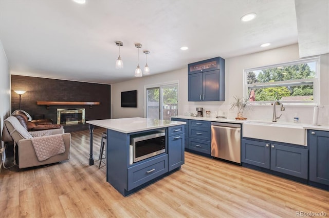 8445 Lamar Dr, Arvada, CO 80003 - kitchen with stainless steel appliances, blue cabinets, open floor plan, a fireplace, and light wood-style flooring
