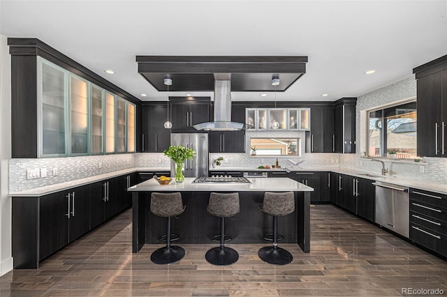 kitchen with a center island, wall chimney range hood, a breakfast bar, stainless steel appliances, and dark cabinets