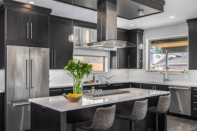 kitchen with island exhaust hood, stainless steel appliances, dark cabinetry, and a sink