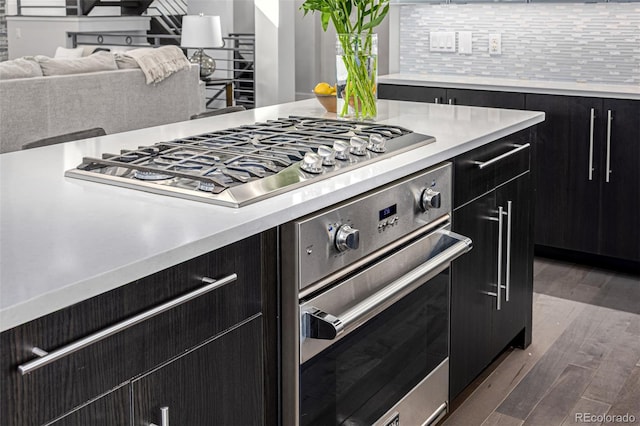 kitchen featuring tasteful backsplash, dark wood-style floors, dark cabinetry, stainless steel appliances, and light countertops